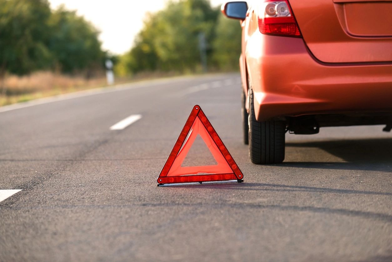 Red warning triangle placed behind a broken-down car on a rural road