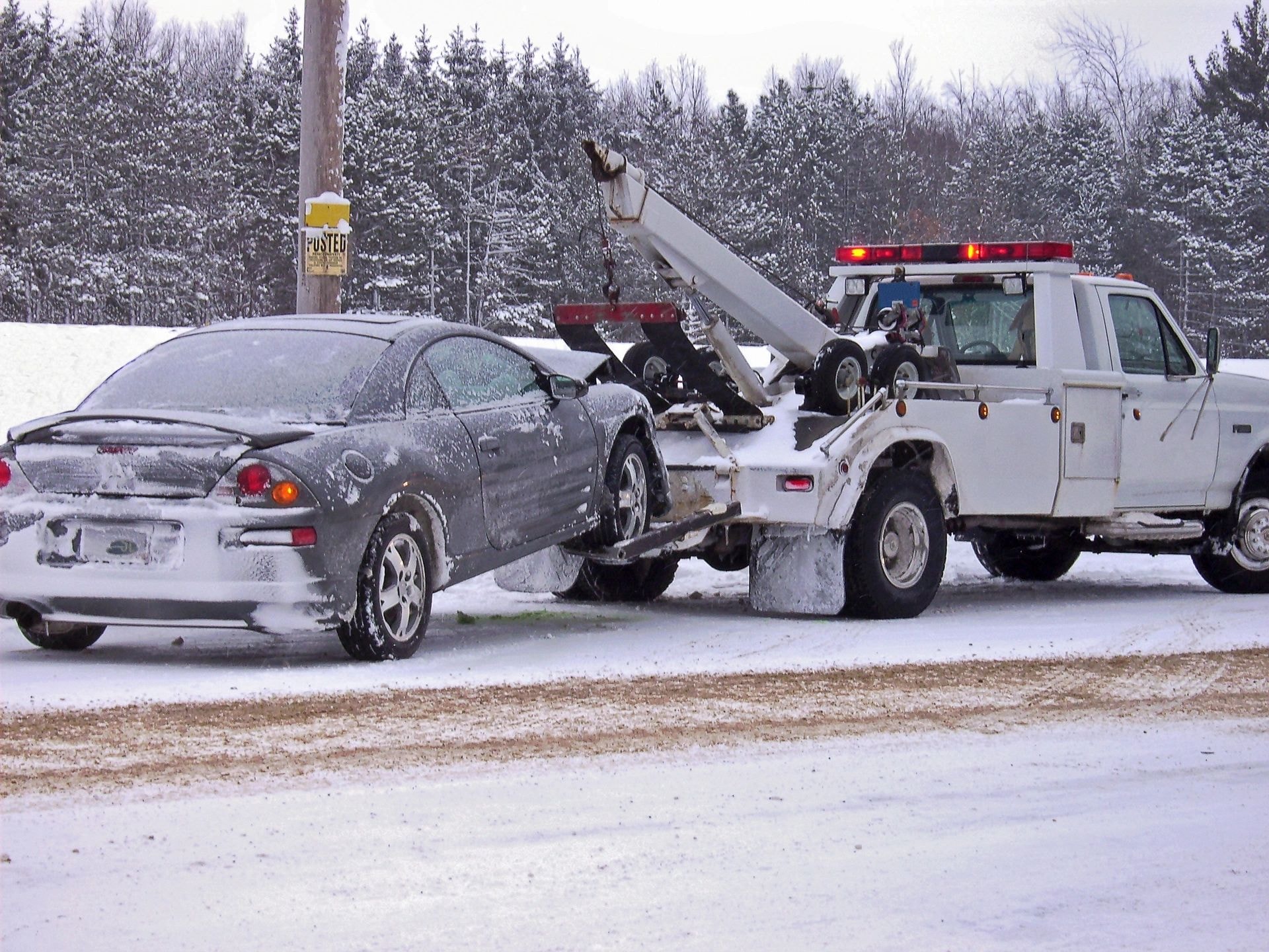 White tow truck towing a snow-covered car in winter conditions