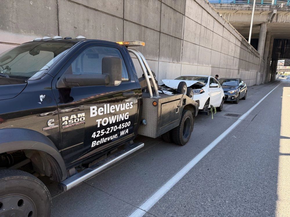 Bellevues Towing flatbed truck carrying a damaged white sedan after an accident
