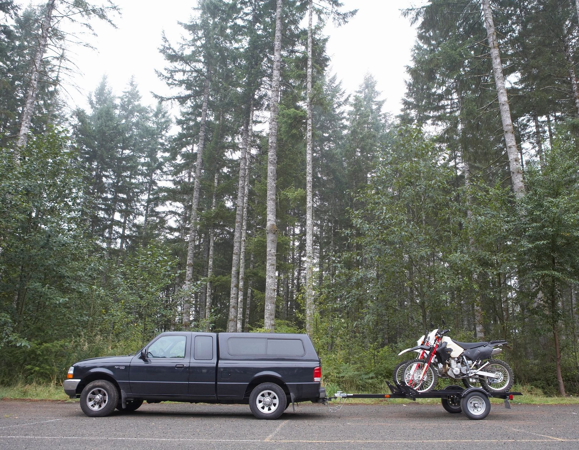 Pickup truck towing a utility trailer with dirt bikes near an evergreen forest