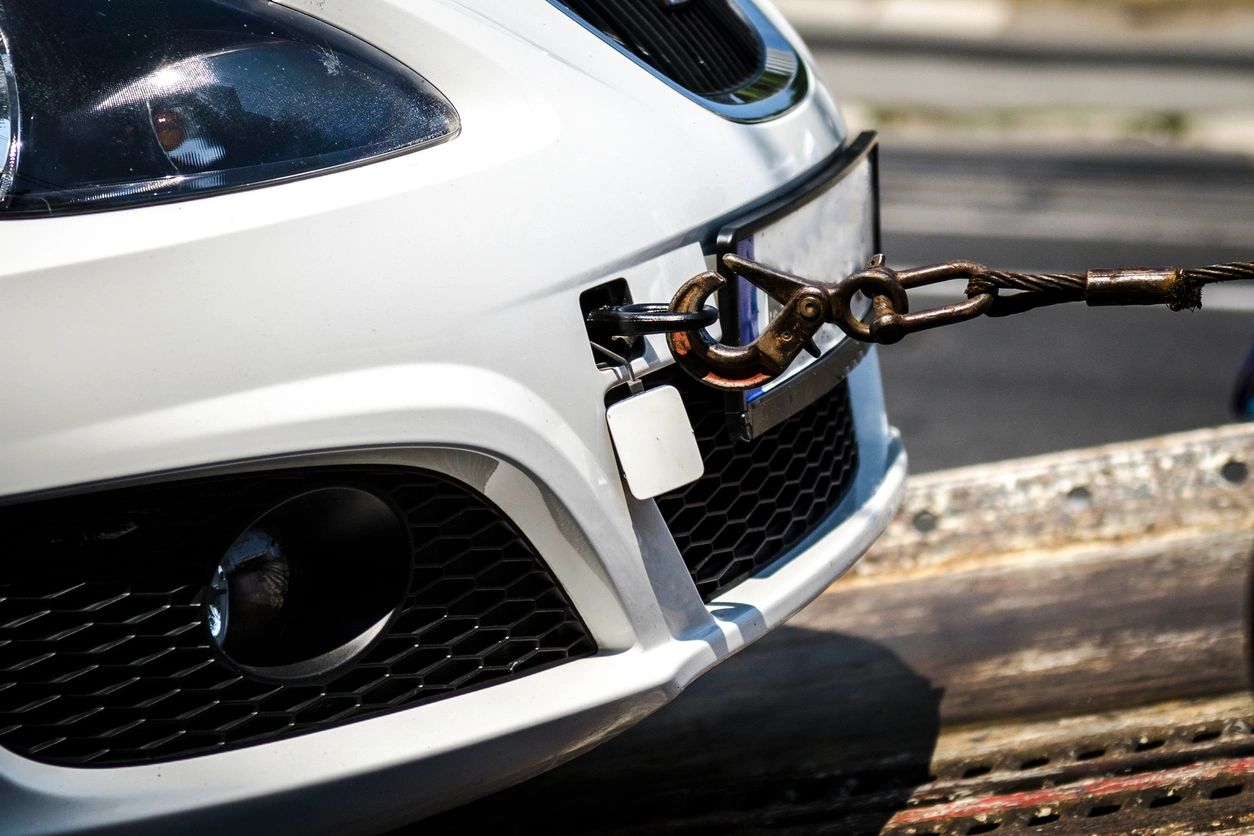 Close-up of the front of a white car being towed with a steel cable and hook