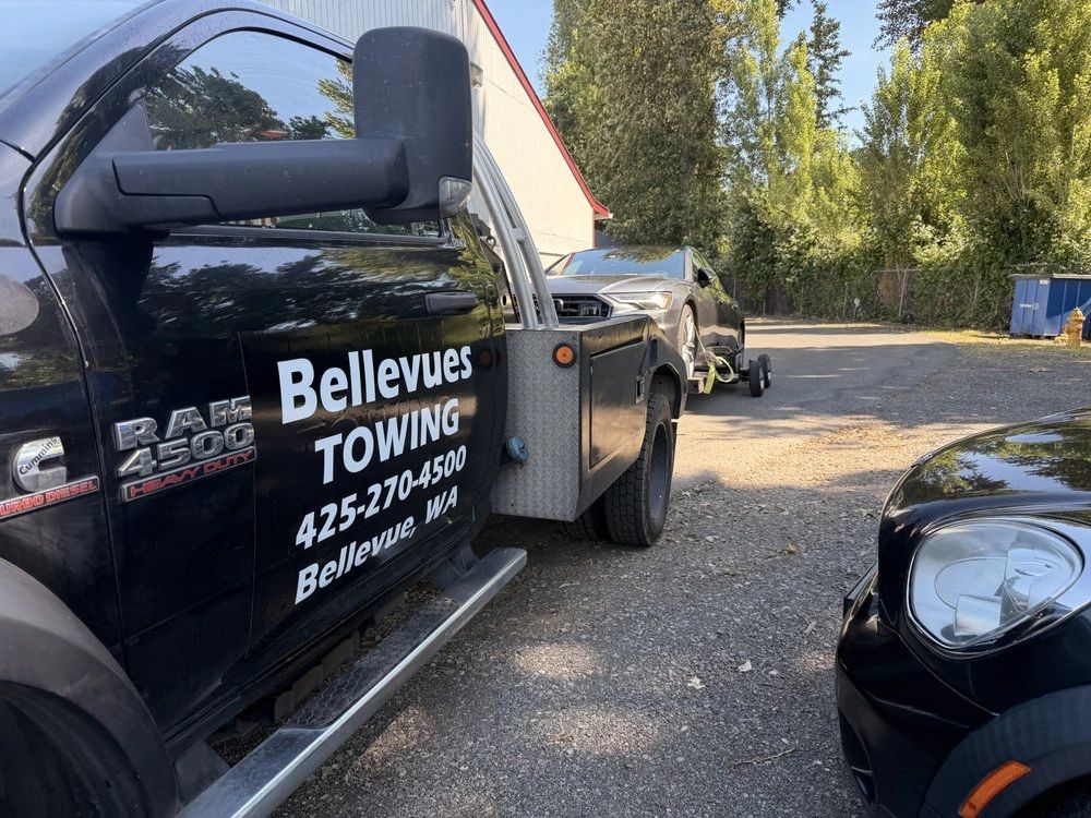 Bellevues Towing flatbed truck towing a dark sedan on a gravel driveway